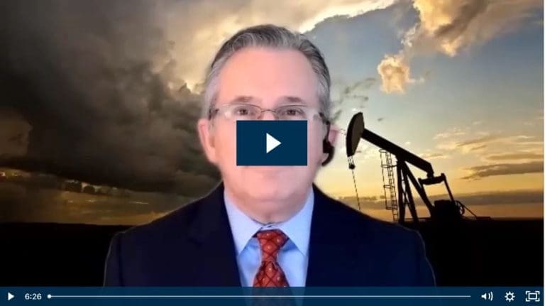 Businessman in a suit discusses oil industry trends with a pumpjack in the background.