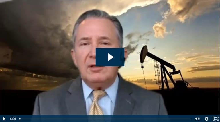 Man in suit discusses oil industry, pumpjack silhouette at sunset in the background.