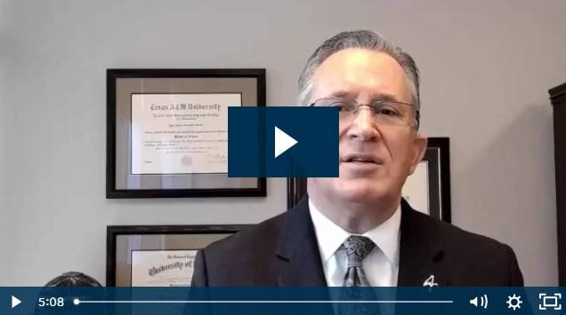 Man in suit speaking in office with framed certificates.