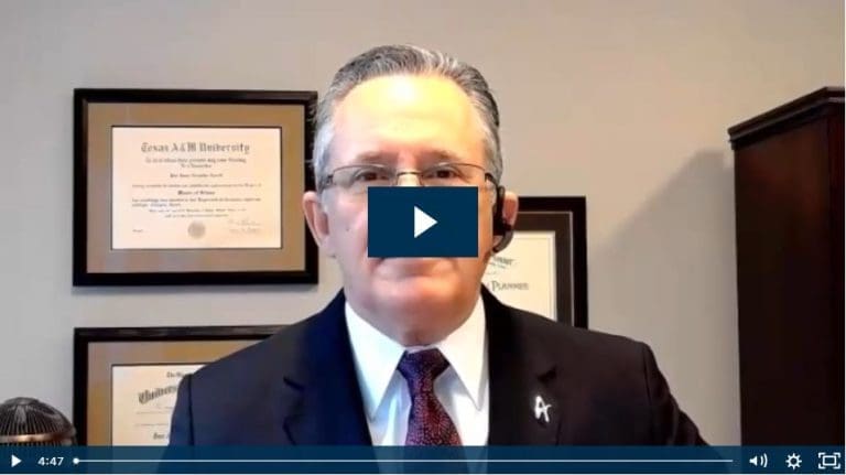 Man in a suit speaking on video call with university diplomas on wall.