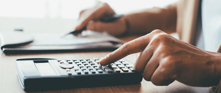 Person using a calculator and pen on a desk for financial work.