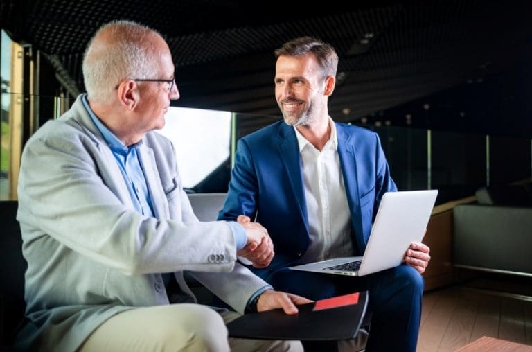 Two businessmen shaking hands during a meeting with a laptop.