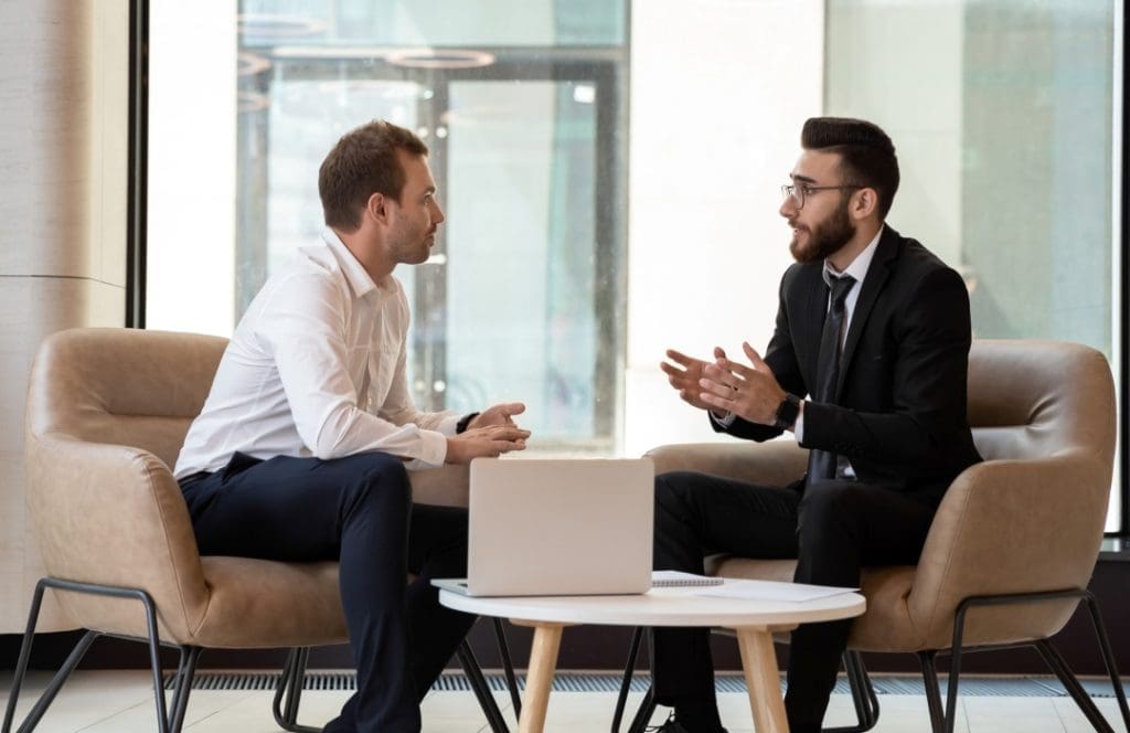 Office meeting between two business professionals seated with a laptop between them.