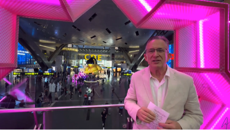 Man in white suit at vibrant airport with giant teddy bear display