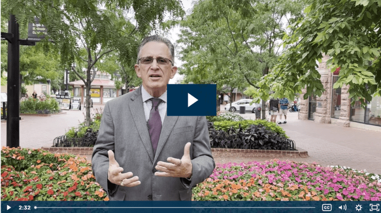 Man in suit speaking in a park with flowers and trees around.