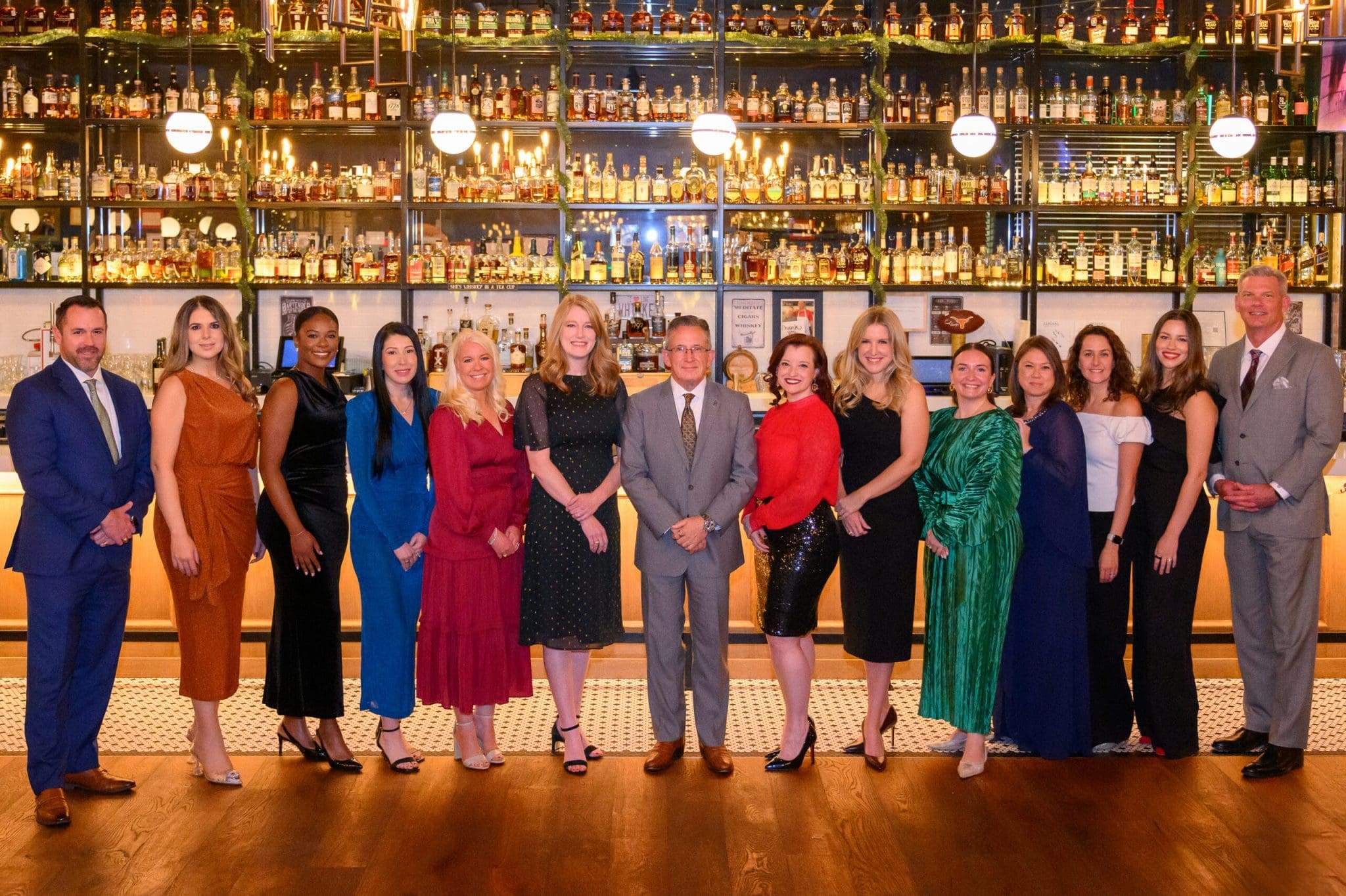 A group of people standing in front of a bar filled with bottles.