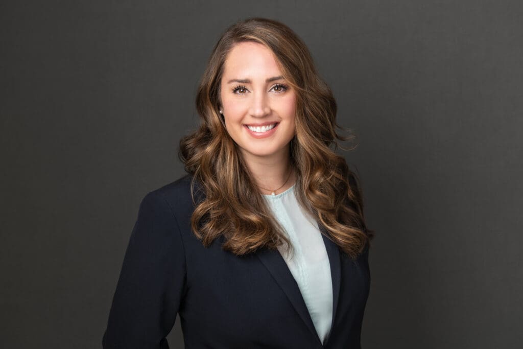 A woman in a professional suit smiles in a studio portrait.