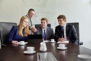 Team meeting in a boardroom with four professionals discussing a project on a laptop.