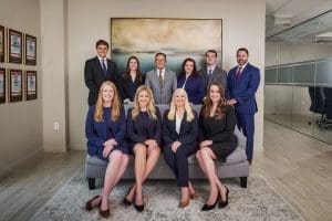 A professional team in formal attire in an office setting, smiling for a group photo.